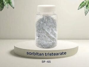 A transparent sample bottle filled with light cream-colored flakes of sorbitan tristearate (SP-65), placed on a white circular podium with text 'sorbitan tristearate SP-65'